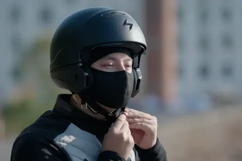 Motocyklista zapina czarną kominiarkę pod kaskiem.