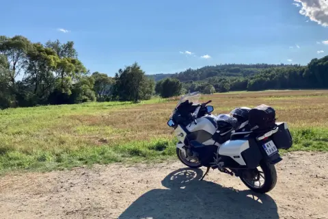 Biały motocykl turystyczny zaparkowany na drodze gruntowej, w tle pole i zalesione wzgórza.