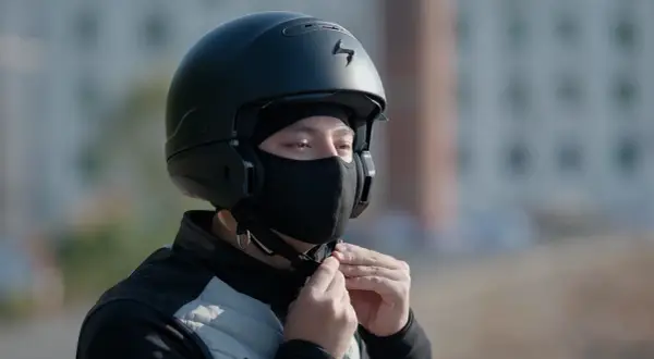 Motocyklista zapina czarną kominiarkę pod kaskiem.