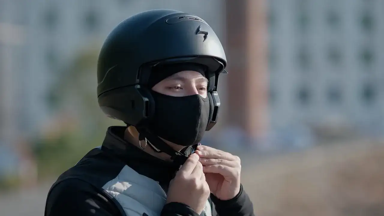 Motocyklista zapina czarną kominiarkę pod kaskiem.